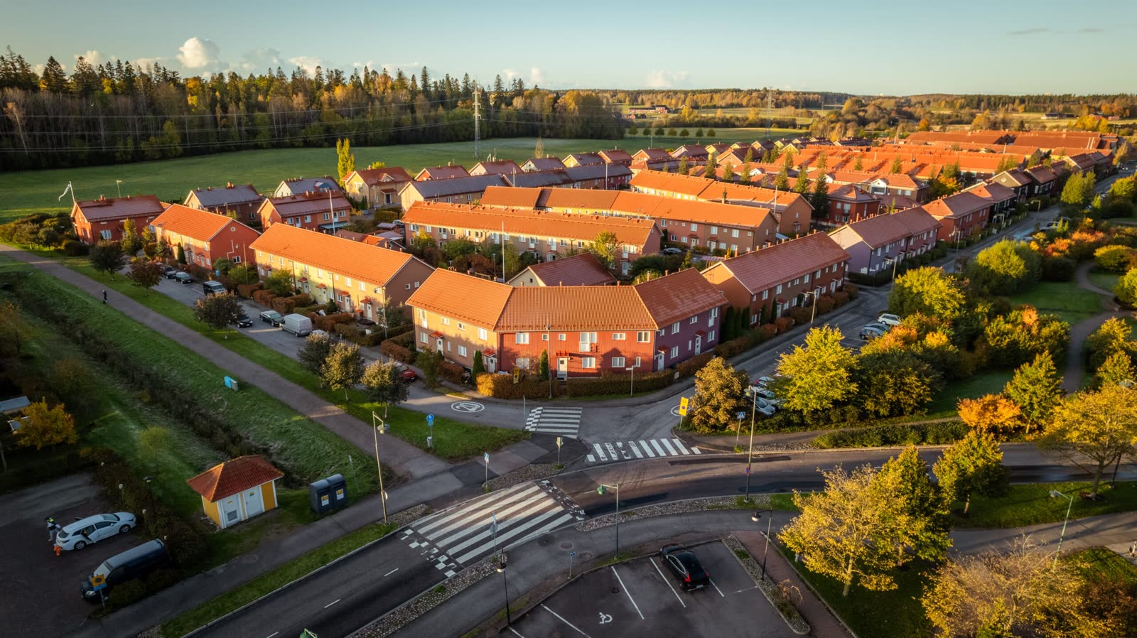 Rekkehus i et borettslag sett fra luften, med tegltak i høstsol